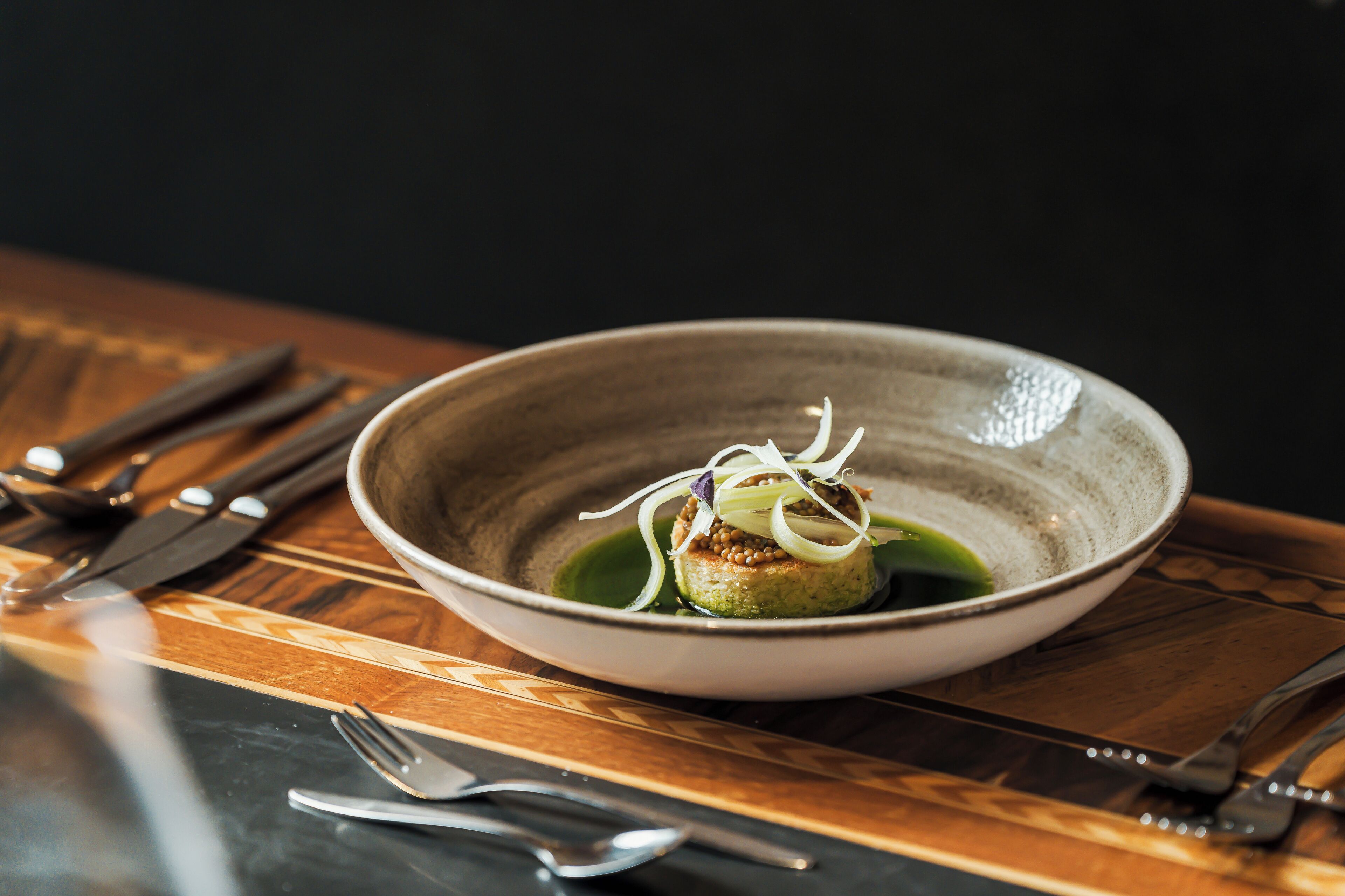 A bowl of food on a table with cutlery around it.