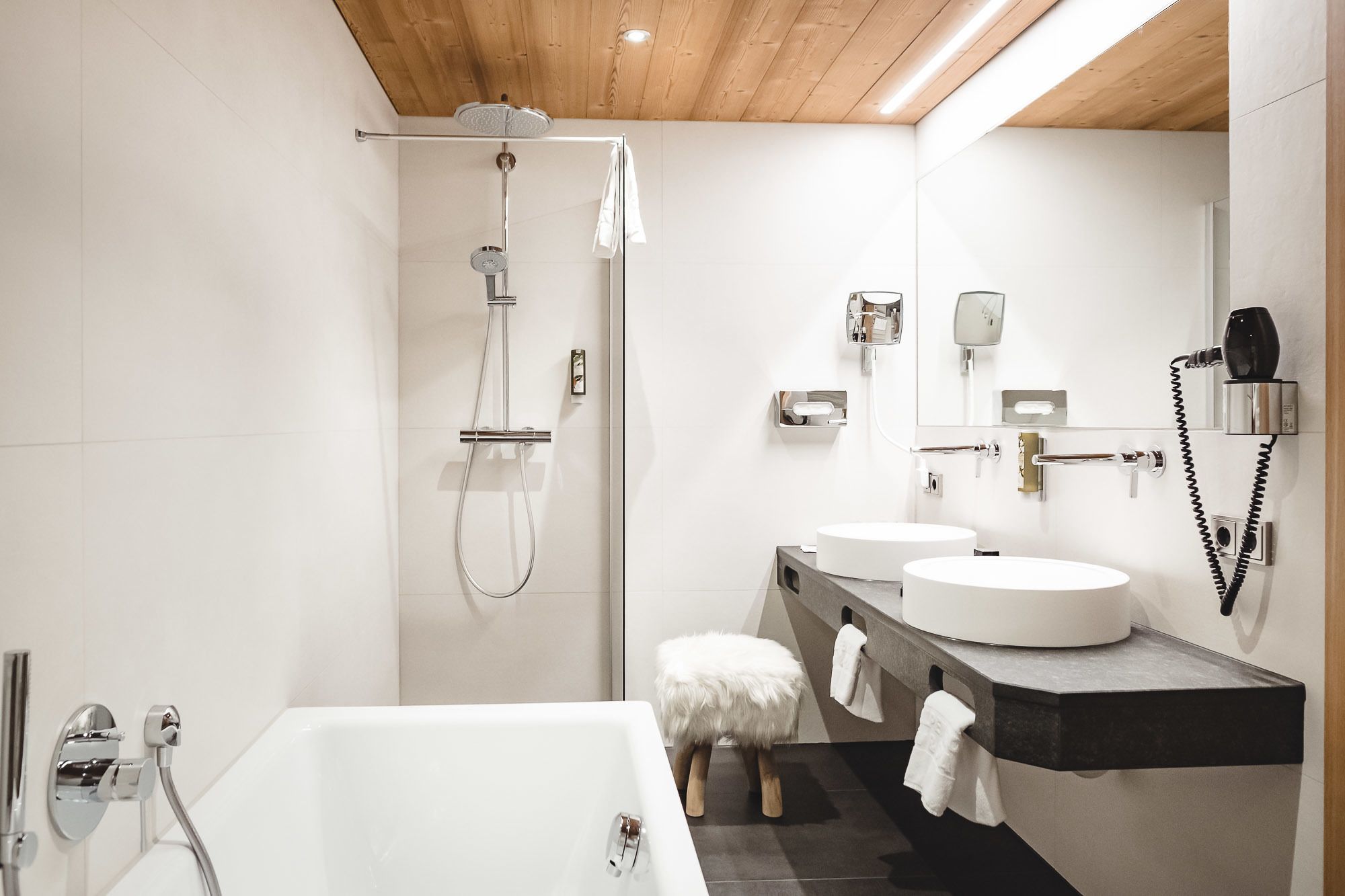 A modern bathroom with a bathtub, two sinks, a shower, and a vanity with a mirror.