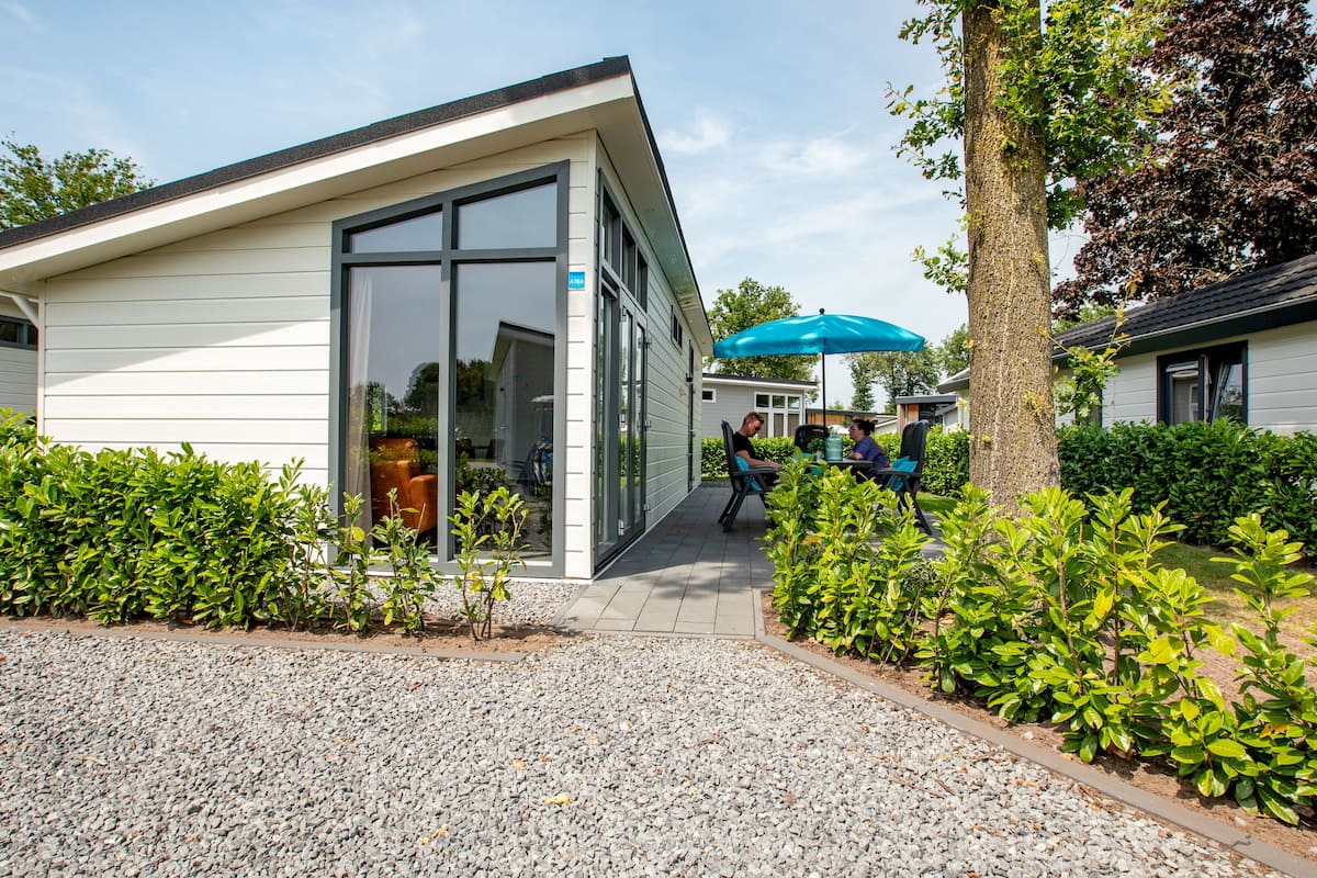 A modern building with a glass entrance, a gravel driveway, and surrounding greenery.