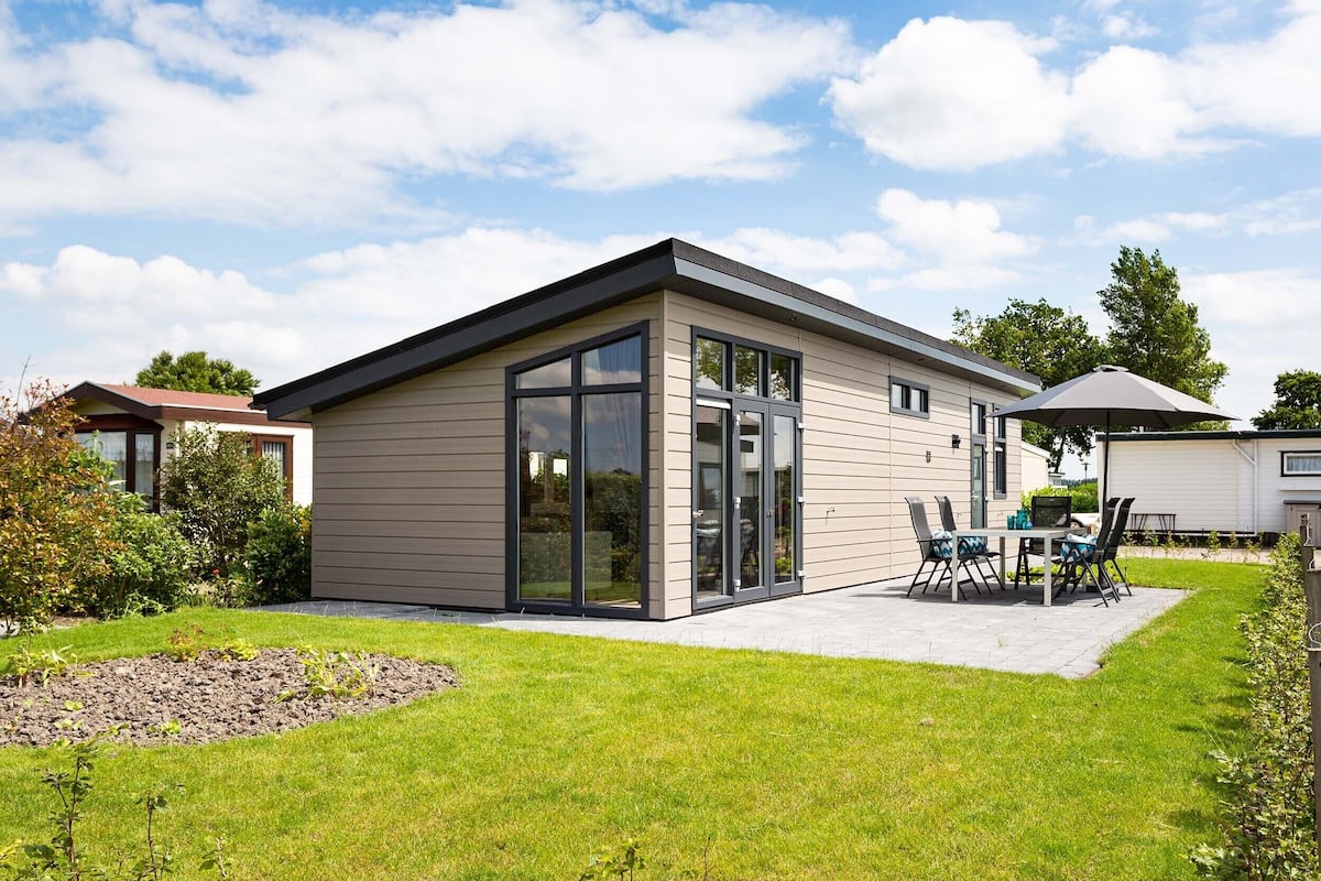 A modern single-story house with a flat roof, large sliding glass doors, and a patio area with outdoor furniture.