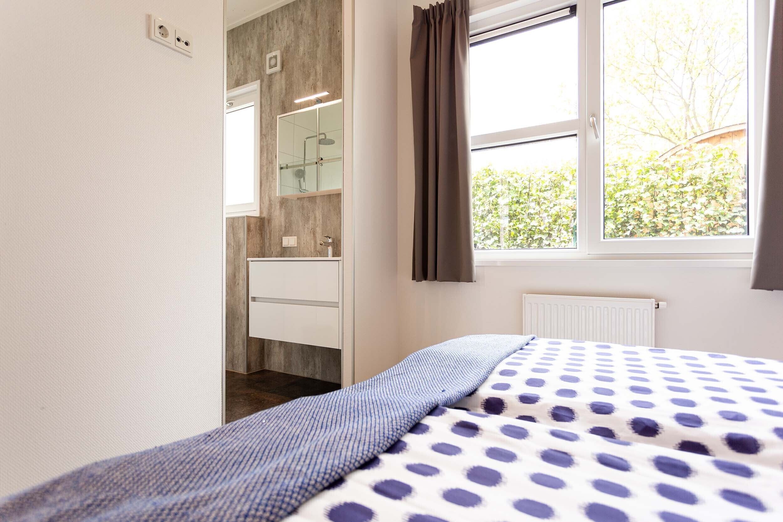 A bedroom with a bed, a window with curtains, a bathroom with a mirror and sink, and a radiator.