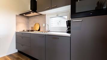 Une cuisine moderne avec des armoires grises, une hotte de cuisinière en acier inoxydable, un four à micro-ondes encastré et une fenêtre au-dessus de l’évier.