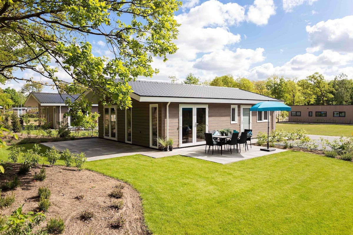 A modern house with a patio, a dining area, and a large lawn.