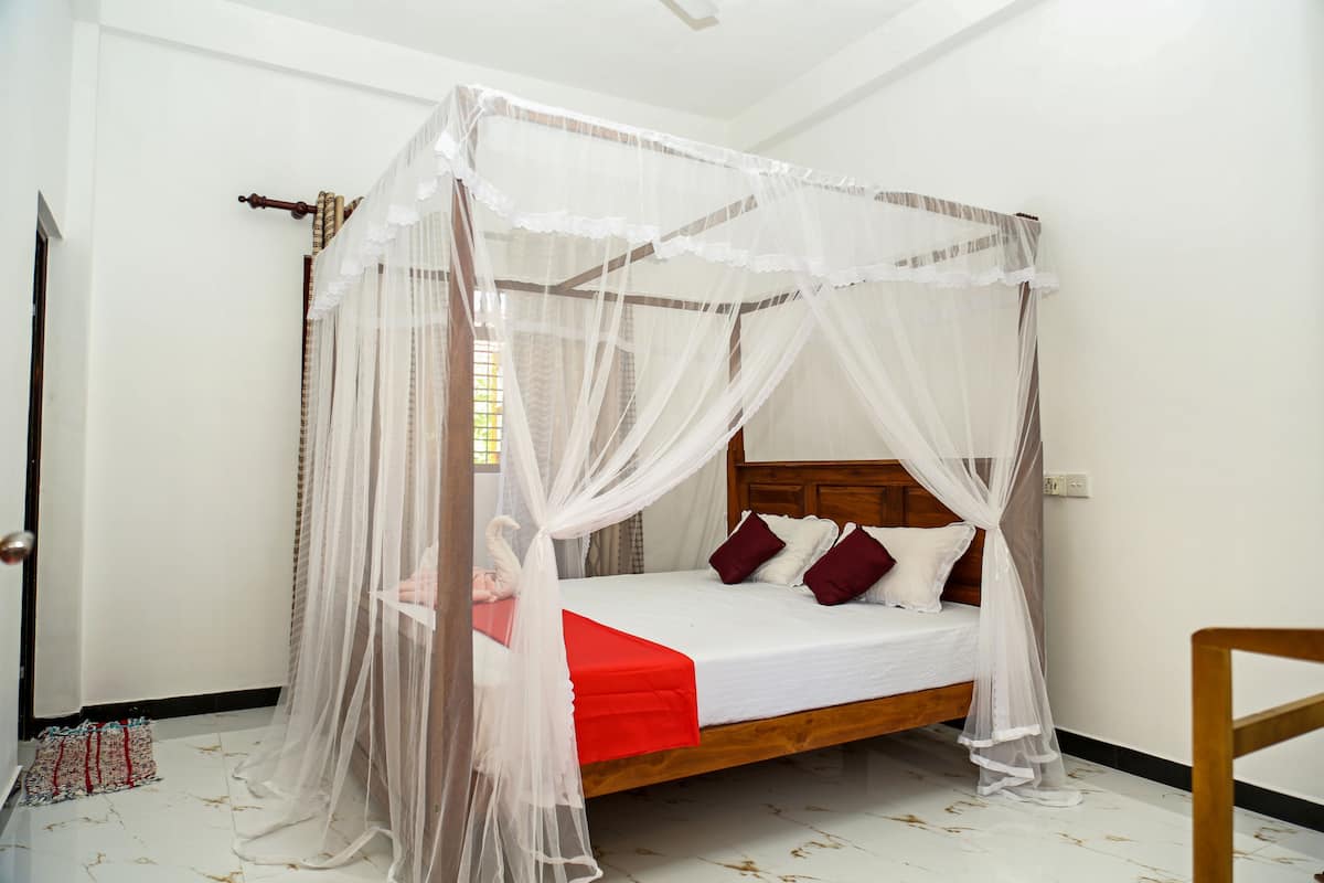 A single bed with a wooden headboard, white bedding, and a red blanket. A white canopy with lace details is draped over the bed.