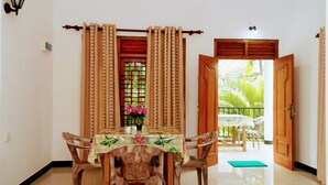 A dining area with a table and chairs, a window with curtains, and a view of the outdoors. - Wayside Guest (Mirissa)
