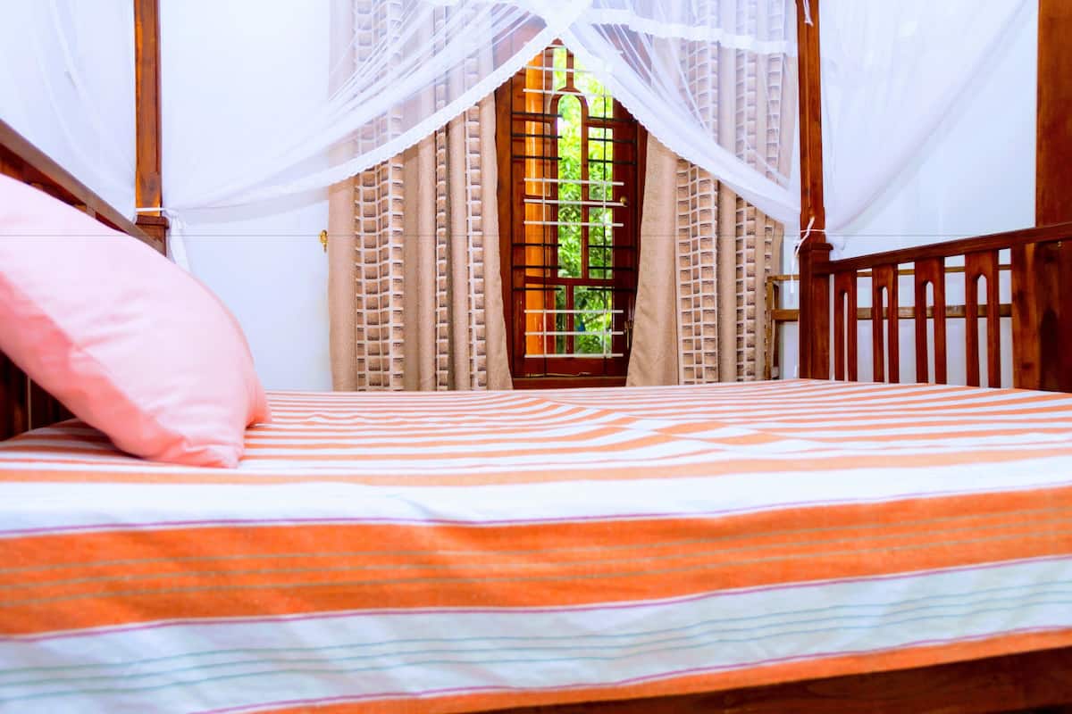 A bed with a striped bedspread, a pink pillow, and a wooden headboard.