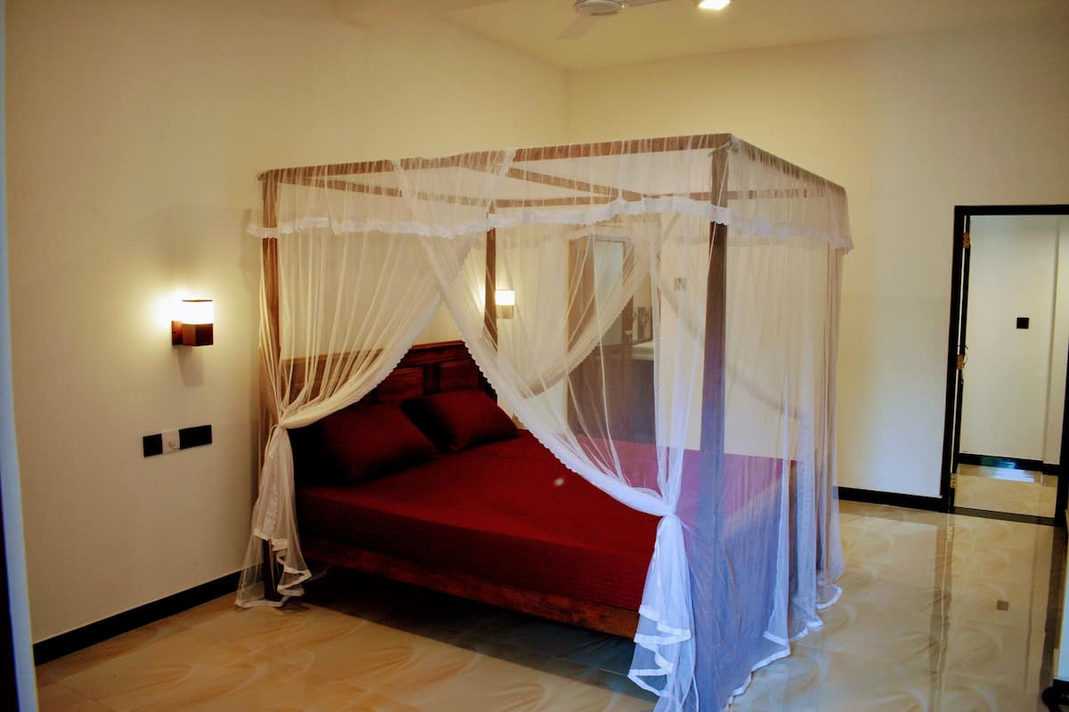 A room with a bed under a canopy, a wall-mounted light, and a mirror.