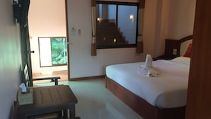A hotel room with a bed, a desk, a window with curtains, and a staircase visible through the window.