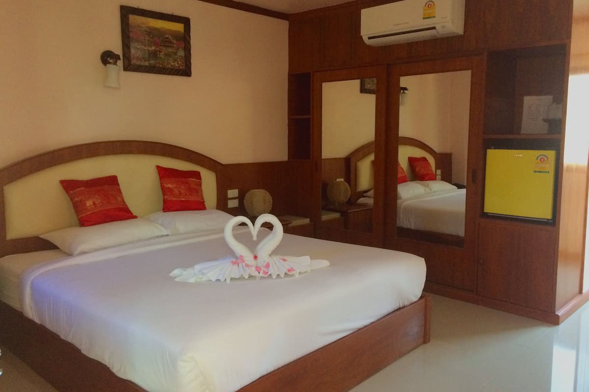 Ein Hotelzimmer mit einem Bett, einem Spiegel, einer Klimaanlage und einem kleinen Tisch mit einer Vase.