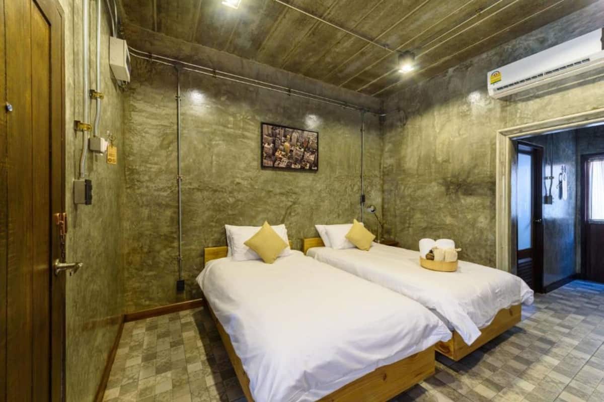 A room with two beds, a wooden door, an air conditioning unit, and a framed picture on the wall.