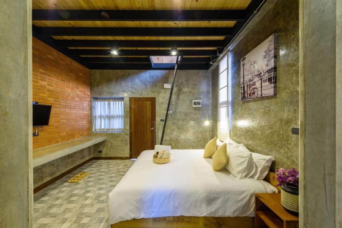 A bedroom with a bed, a wooden bench, a window with curtains, a brick wall, and a mounted picture.