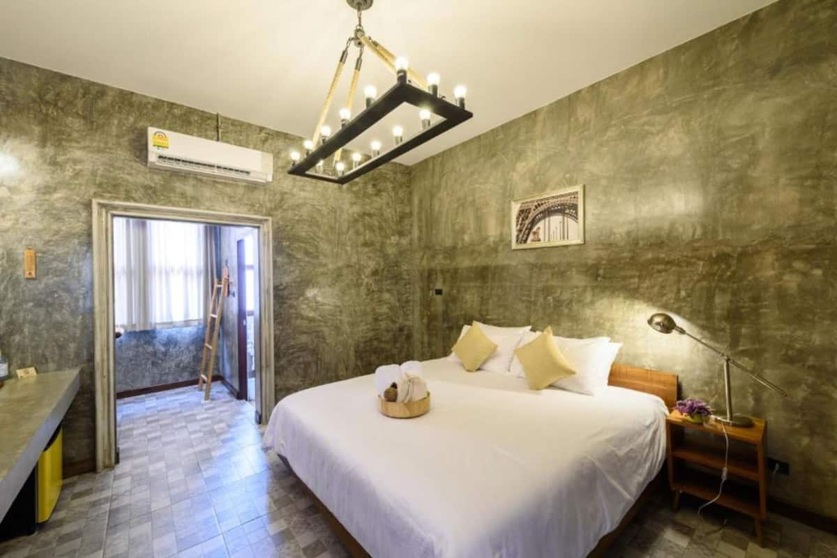 A hotel room with a large bed, a desk, and a chair. There is a window with curtains, a door, and a wall-mounted air conditioner.