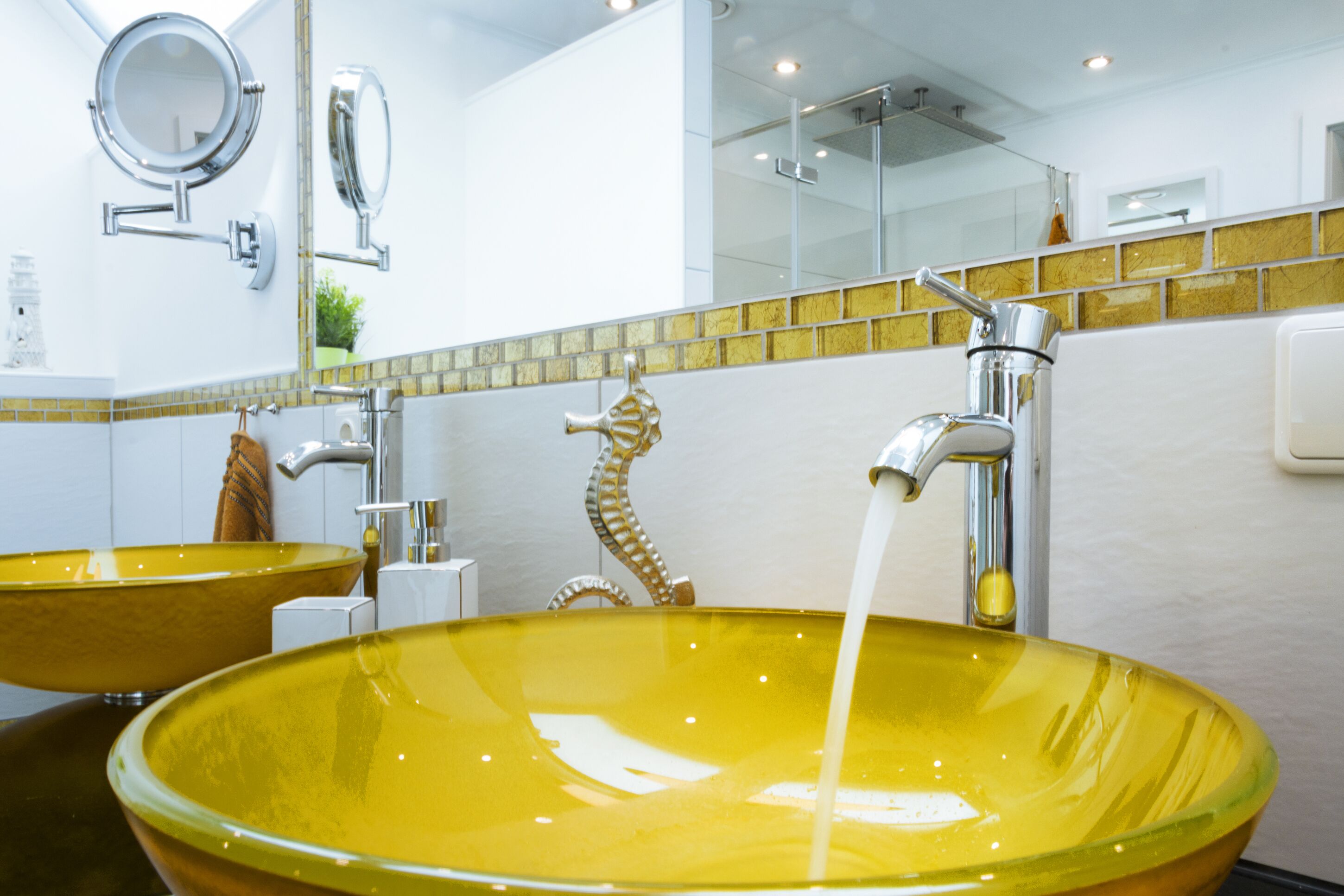 Un baño con dos lavamanos de vidrio amarillo, un espejo y un perchero para toallas.