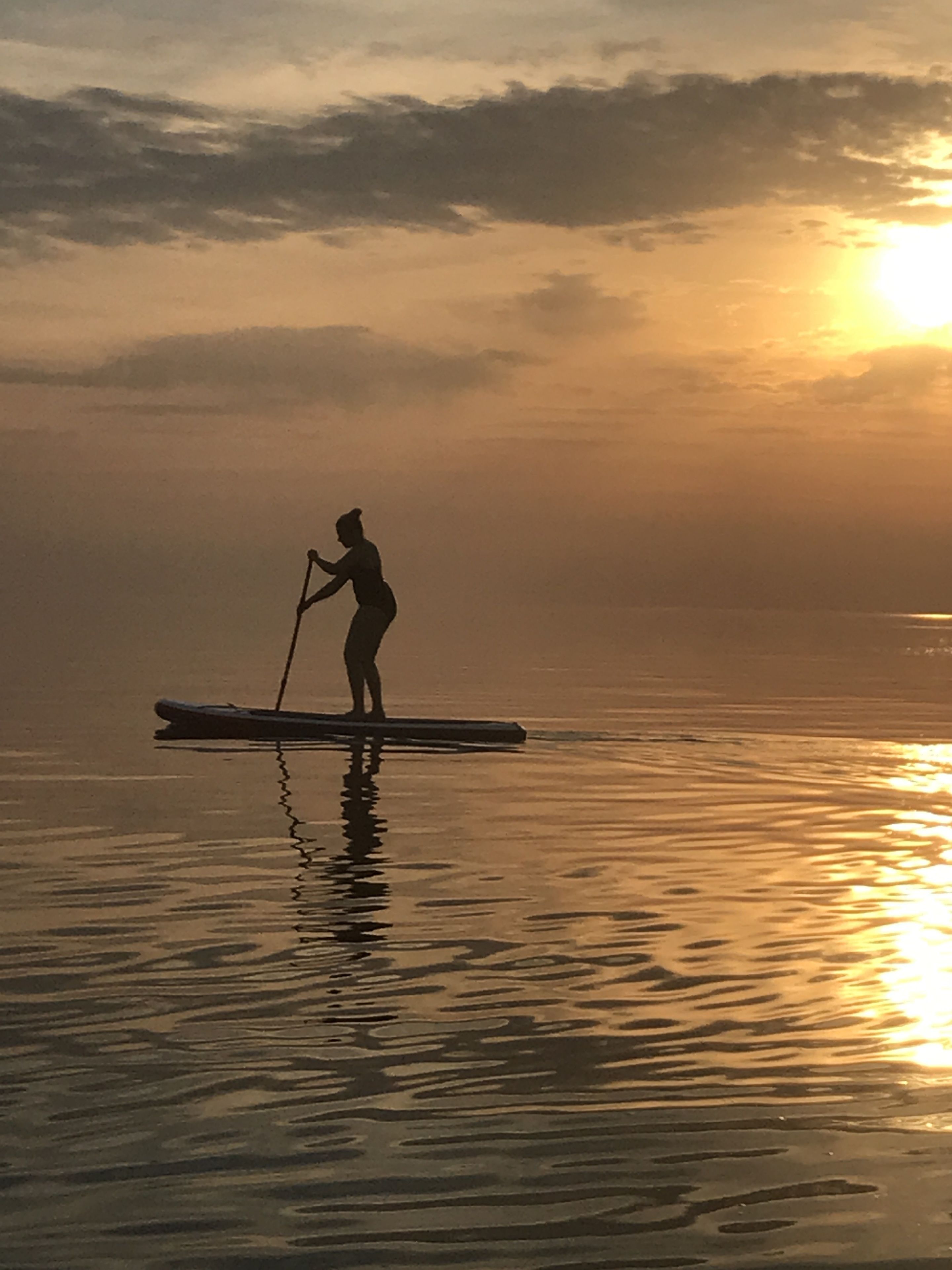 Una persona haciendo paddleboard en aguas tranquilas durante el atardecer.