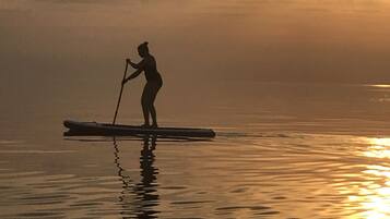Una persona haciendo paddleboard en aguas tranquilas durante el atardecer.
