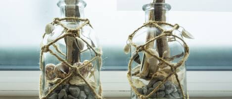 Deux bouteilles en verre, décorées de ficelle et de coquillages, sont posées sur un rebord de fenêtre.