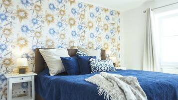 Een slaapkamer met bloemenbehang, een blauw beddegoed en een nachtkastje met een lamp.