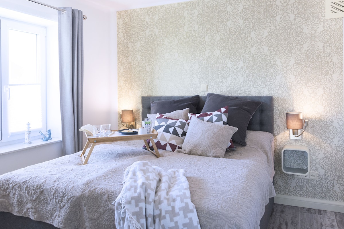 A neatly made bed with a patterned bedspread, pillows, and a bedside table with a lamp and a book.