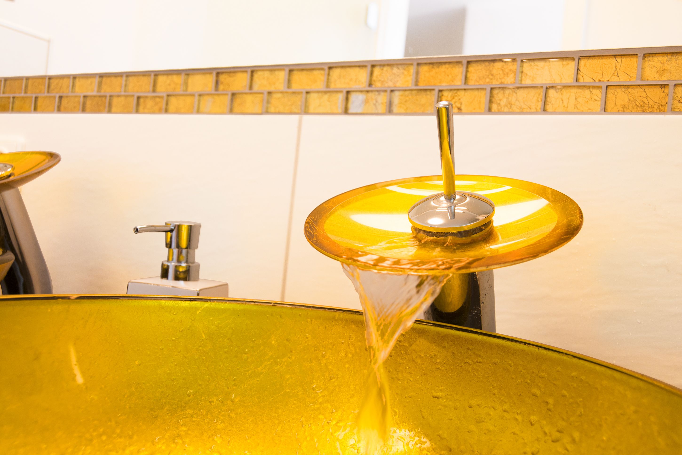 A yellow glass basin with water flowing from a faucet.