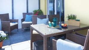 Un patio con mobiliario de mimbre, una mesa de vidrio y plantas en macetas.