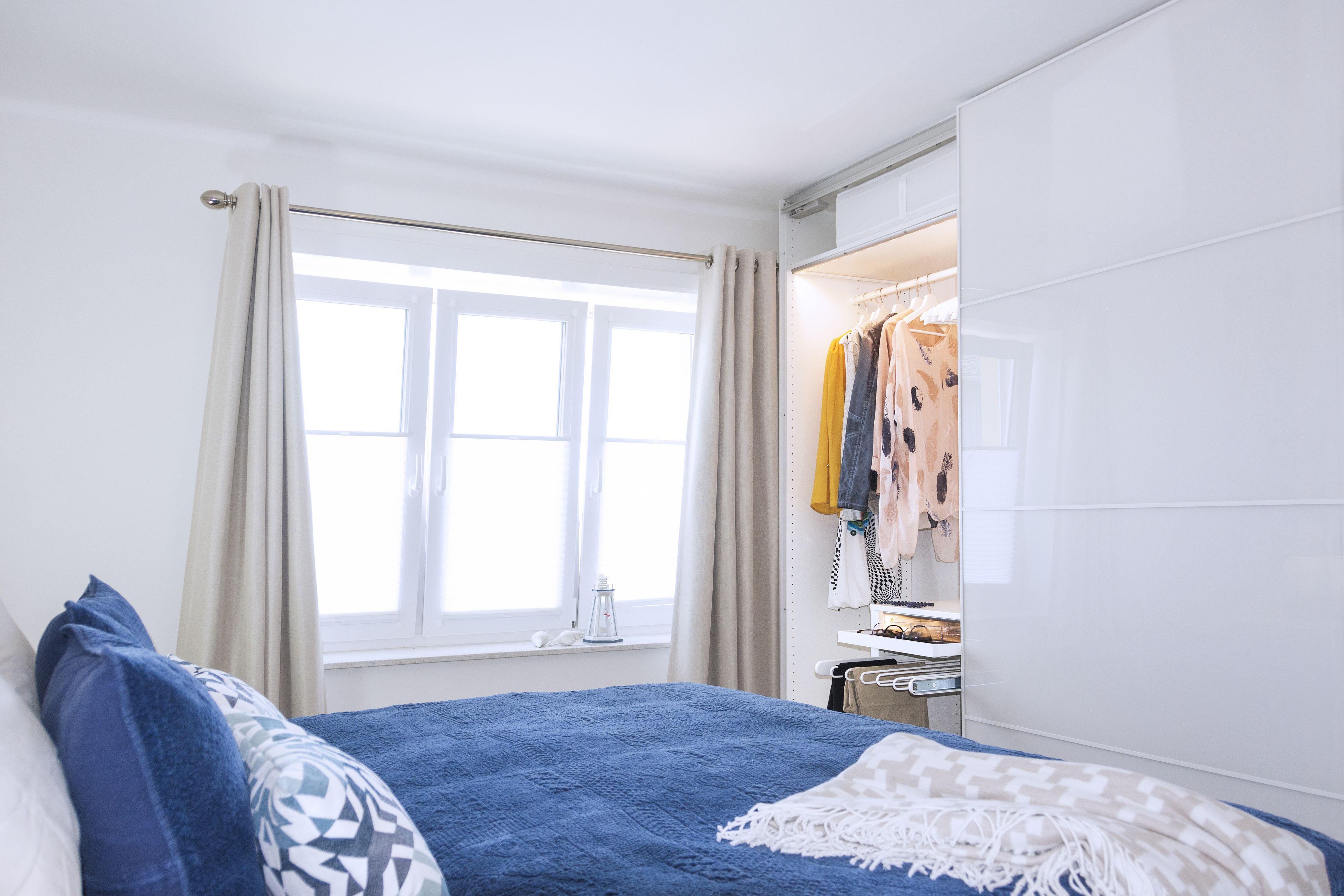 Ein Schlafzimmer mit Bett, einem Fenster mit Vorhängen, einem Kleiderschrank und einem Nachttisch.