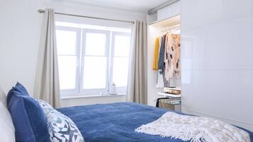 Ein Schlafzimmer mit Bett, einem Fenster mit Vorhängen, einem Kleiderschrank und einem Nachttisch.