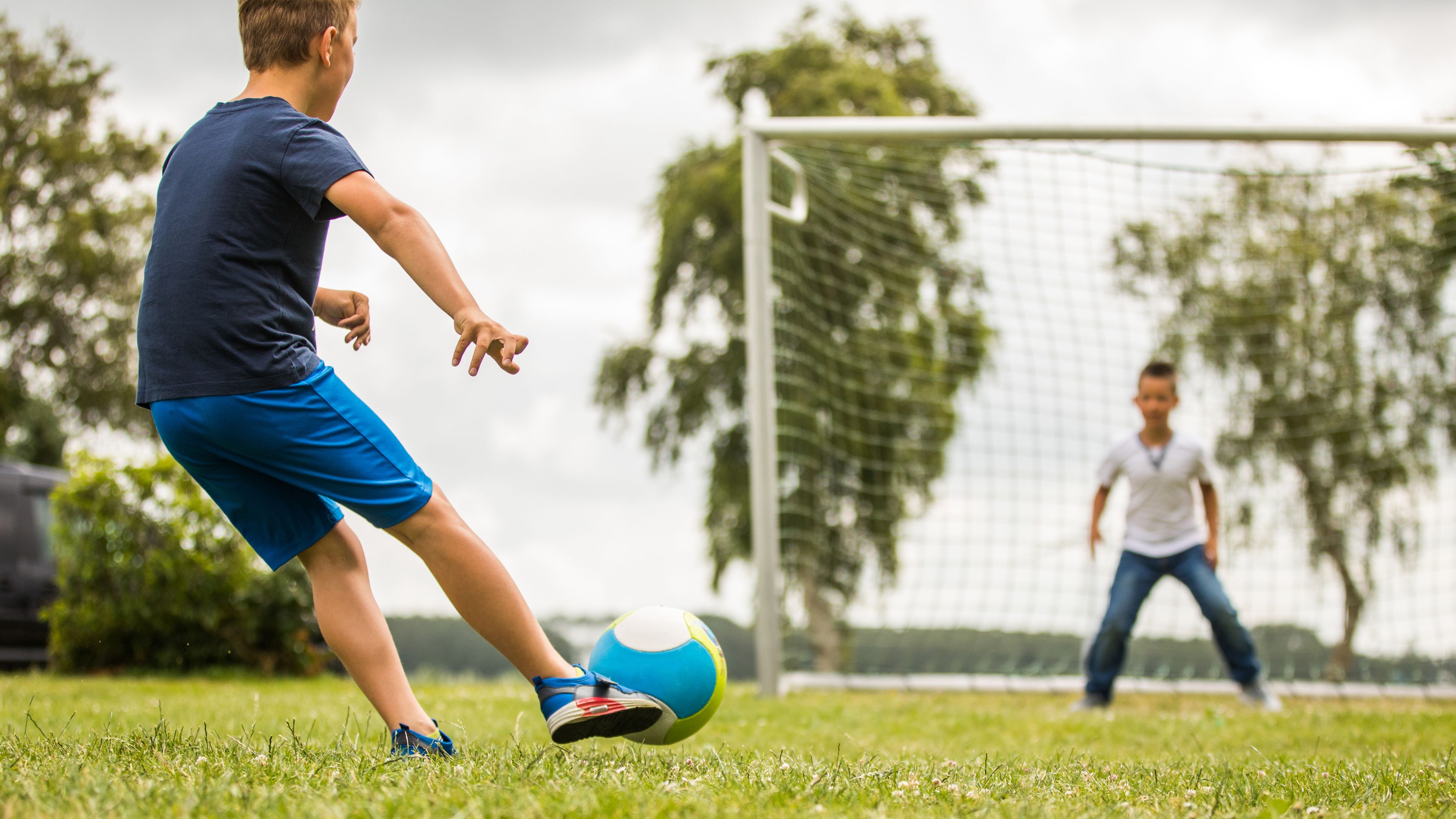 Un match de football est en cours sur un terrain herbeux, avec un poteau de but en arrière-plan.