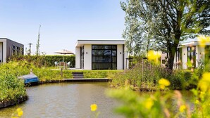 Een modern gebouw met grote ramen, een smal waterkanaal en veel groen eromheen.