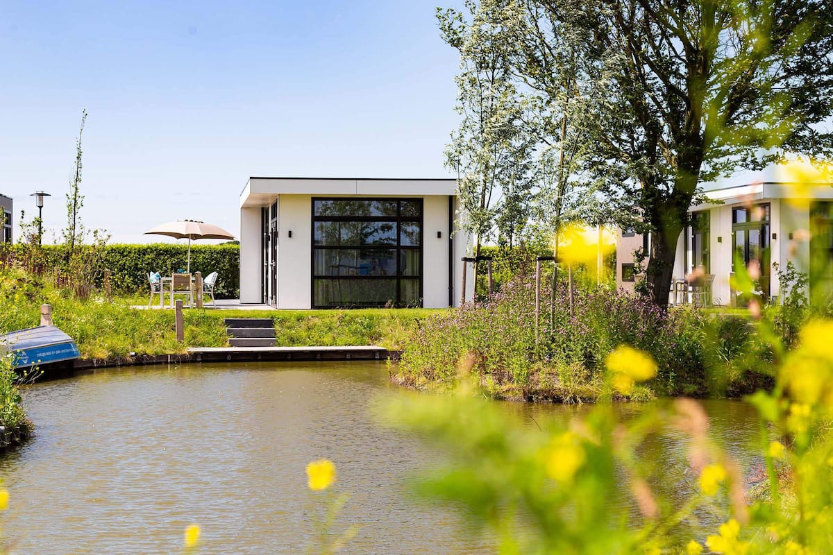 Un edificio moderno con amplios ventanales, un pequeño canal de agua y vegetación circundante.