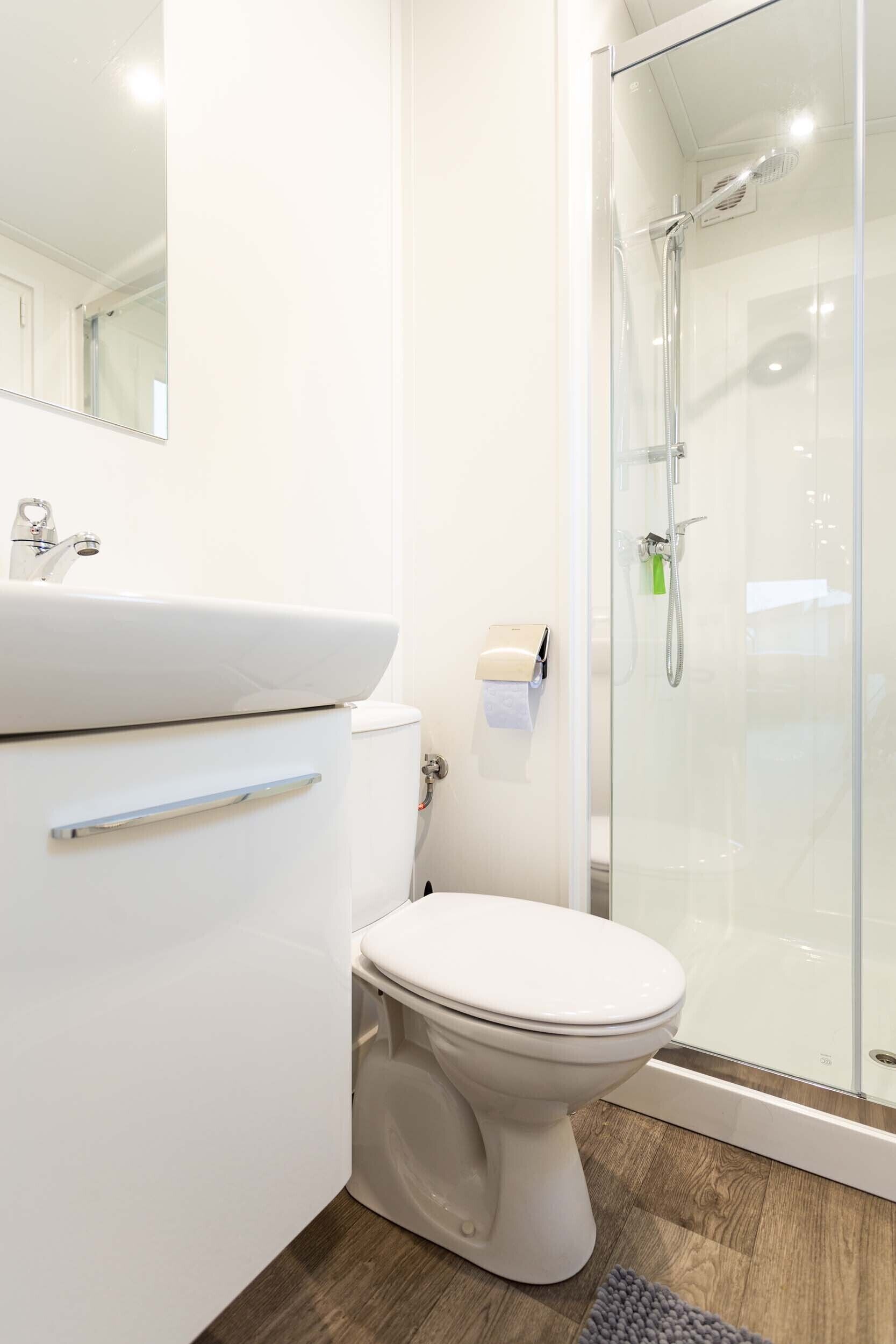 A modern bathroom with a white sink, toilet, and glass shower enclosure.