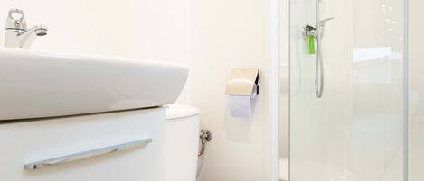 A modern bathroom with a white sink, toilet, and glass shower enclosure.
