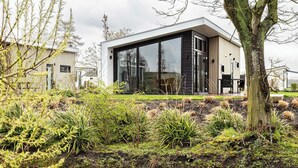 Een modern gebouw met grote glasramen, een plat dak en een aangelegde tuin met een vijver.