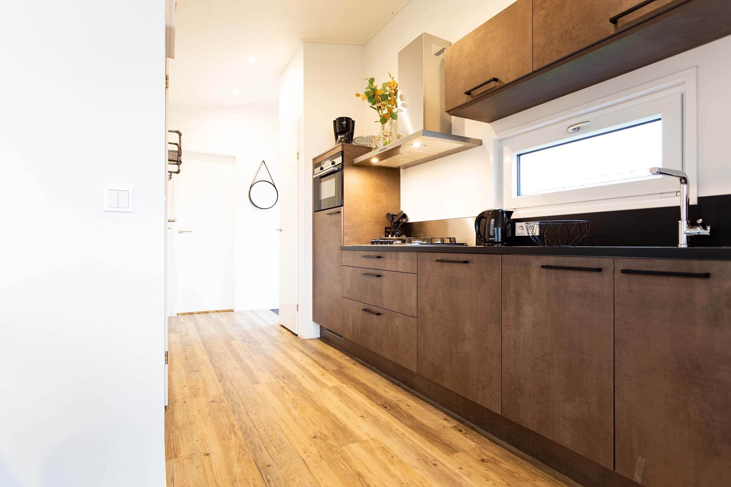 Een moderne keuken met houten kastjes, een inbouwoven en een raam boven de spoelbak.