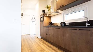 Een moderne keuken met houten kastjes, een inbouwoven en een raam boven de spoelbak.