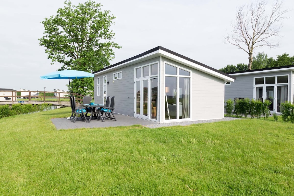 Una casa moderna con un patio, una mesa de comedor y una sombrilla azul.