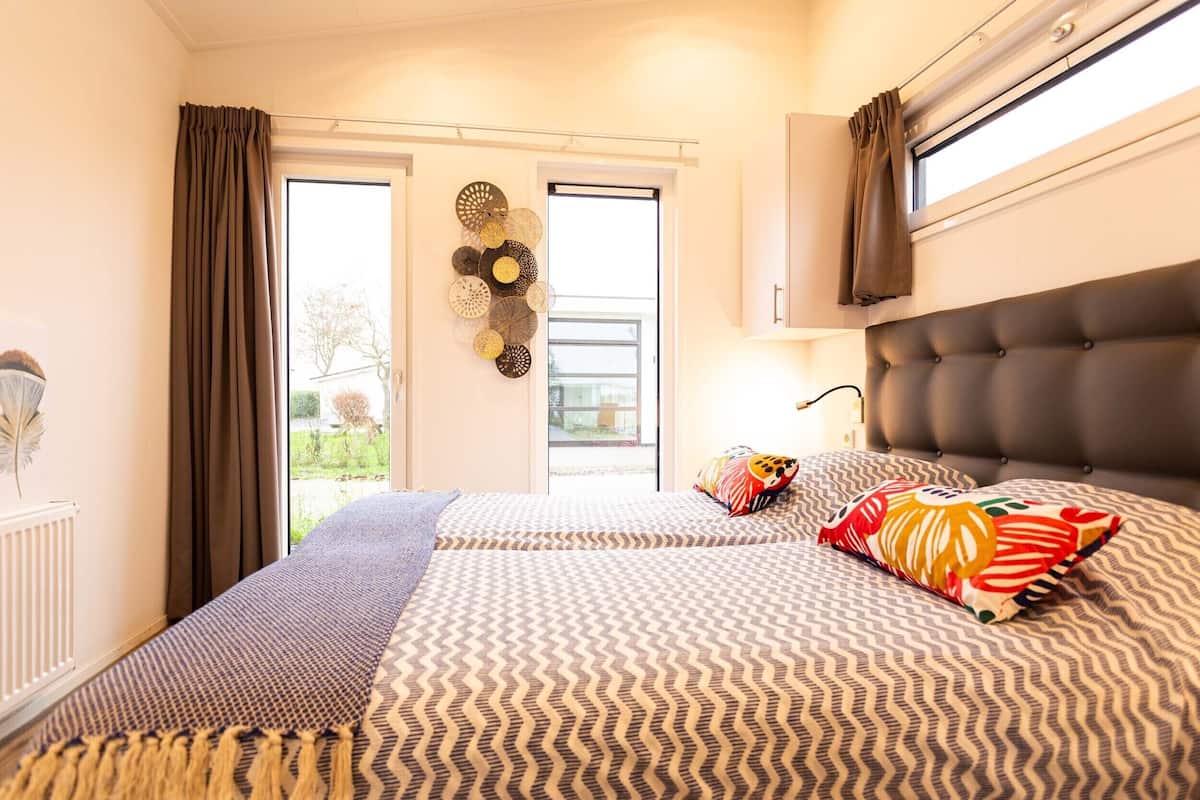 Un dormitorio con una cama grande, una ventana con cortinas, un radiador y una lámpara fijada a la pared.