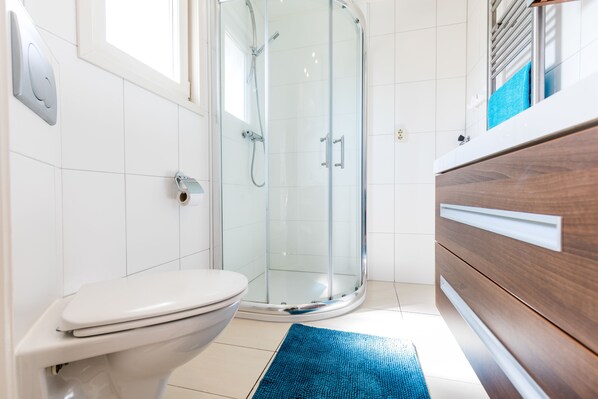 Un baño moderno con cabina de ducha de vidrio, inodoro blanco y tocador de madera.