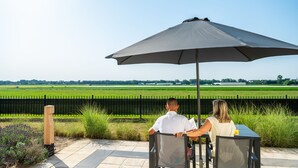 Una pareja sentada en una mesa al aire libre con una sombrilla grande, con vista a un campo verde.