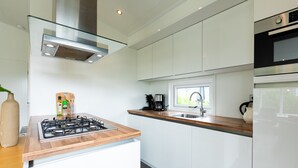 Una cocina moderna con armarios blancos, encimera de madera, estufa a gas, campana extractora de acero inoxidable, ventana y horno empotrado.