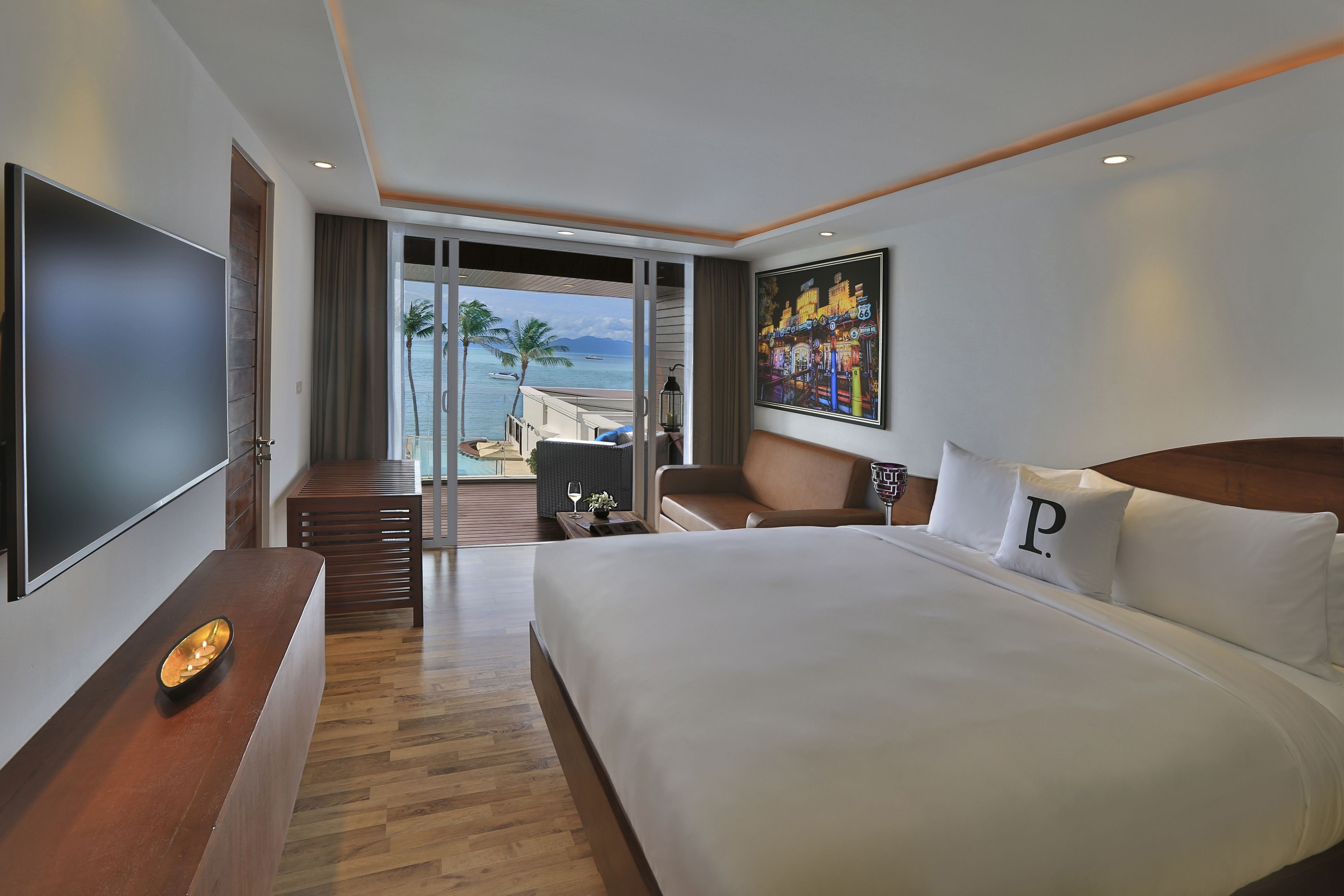 Een hotelkamer met een groot bed, een flatscreen televisie, een houten bureau en een balkon met uitzicht op de oceaan.