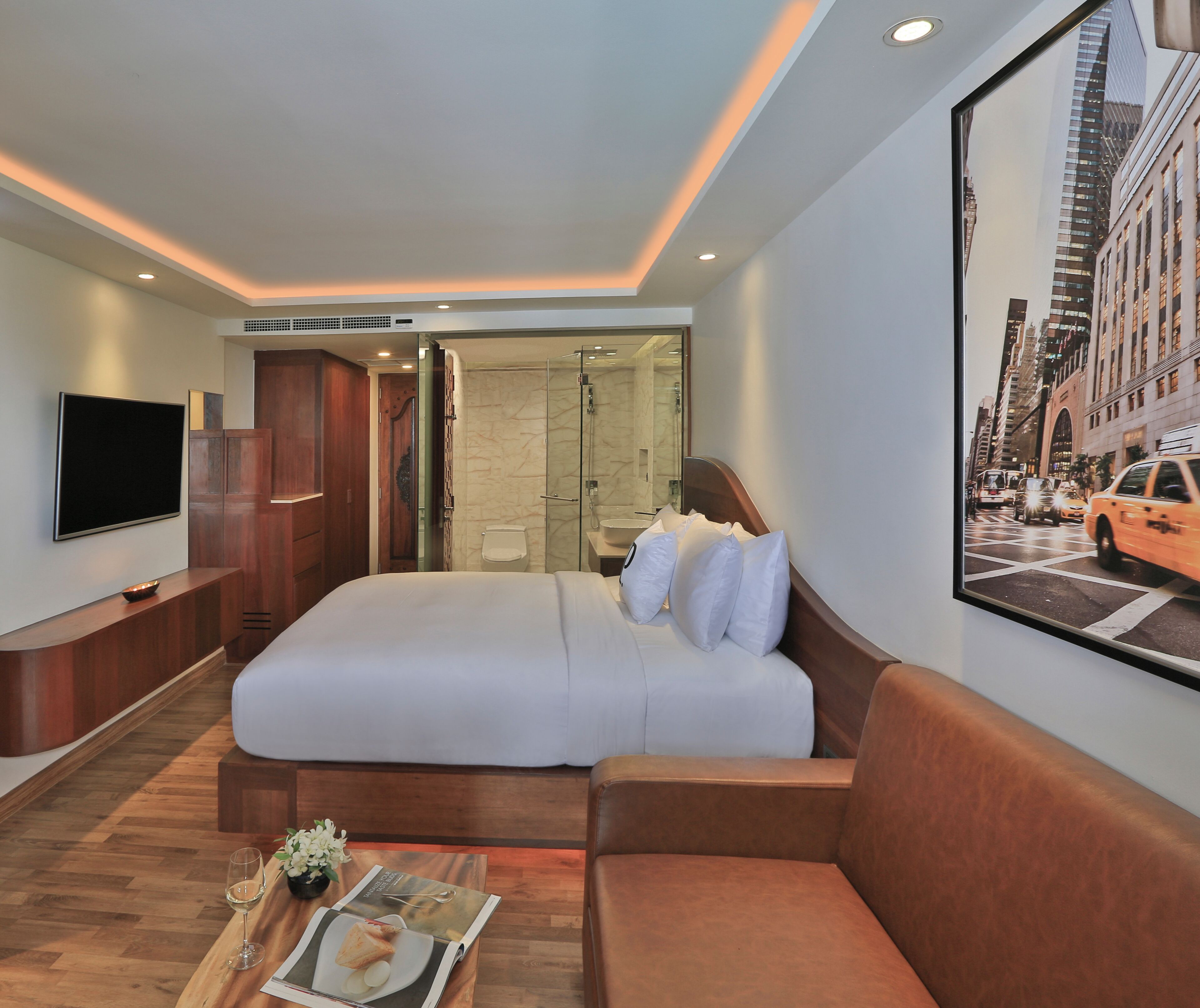 A hotel room with a large bed, a TV, a glass-enclosed shower, and a cityscape view.