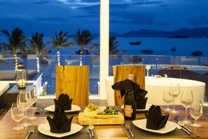 A dining table set with plates, cutlery, and wine glasses, overlooking a body of water with boats and palm trees. - The Privilege Hotel Ezra Beach Club (Koh Samui)