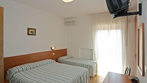 Une chambre d’hôtel avec deux lits simples, une tête de lit en bois, une petite table, un projecteur fixé au mur et une fenêtre avec des rideaux.