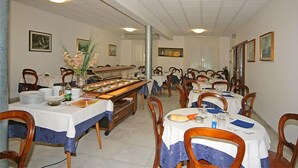 Un espace repas avec plusieurs tables dressées pour les repas, des chaises et un buffet.