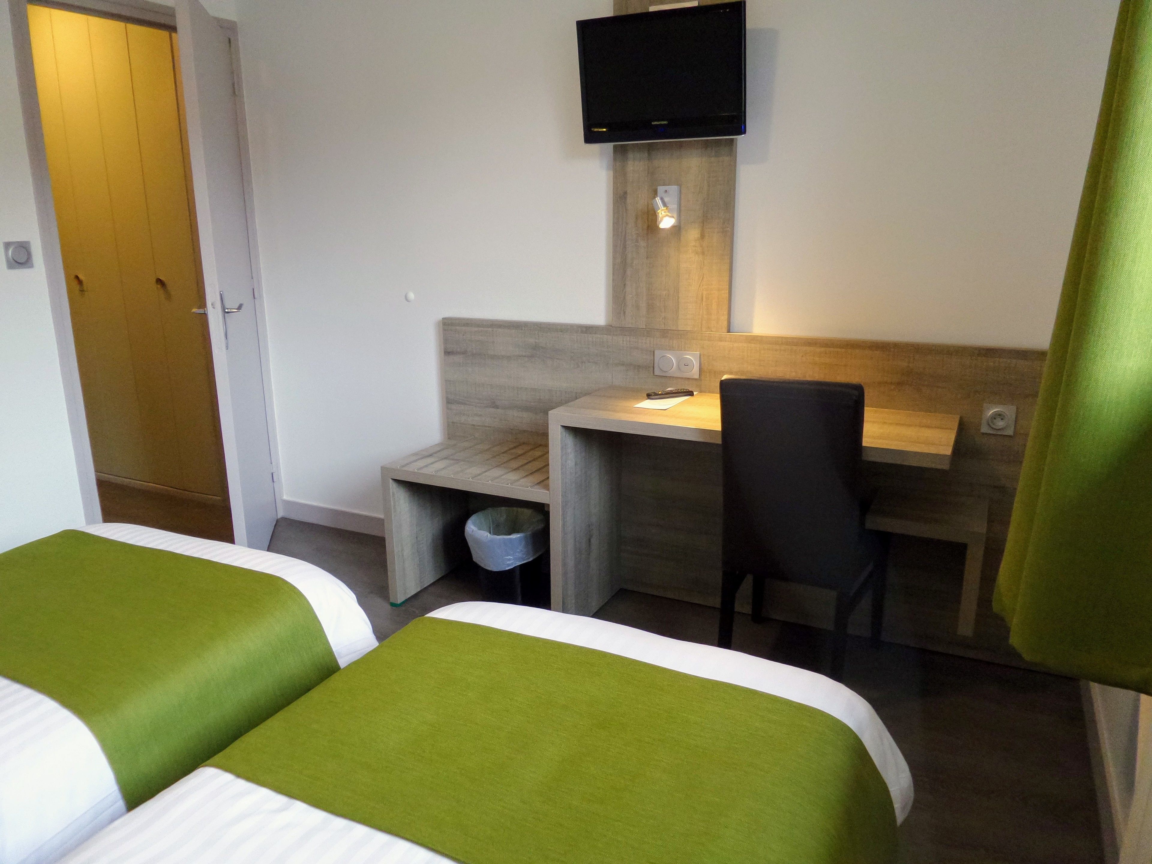 Habitación de hotel con dos camas, un escritorio, una silla, un televisor y un cesto de basura.