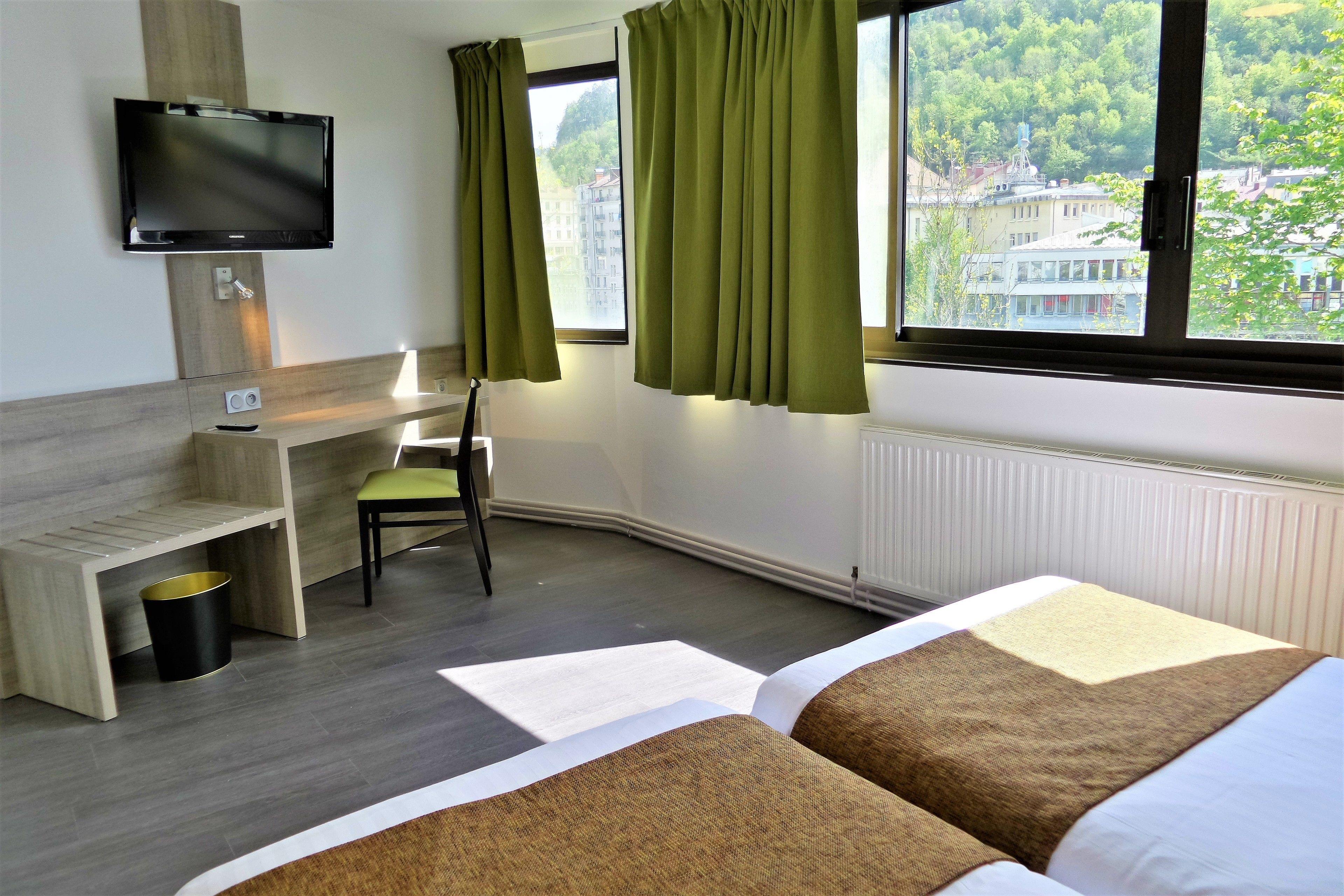 Habitación de hotel con cama, escritorio, silla, televisor y ventana con cortinas.
