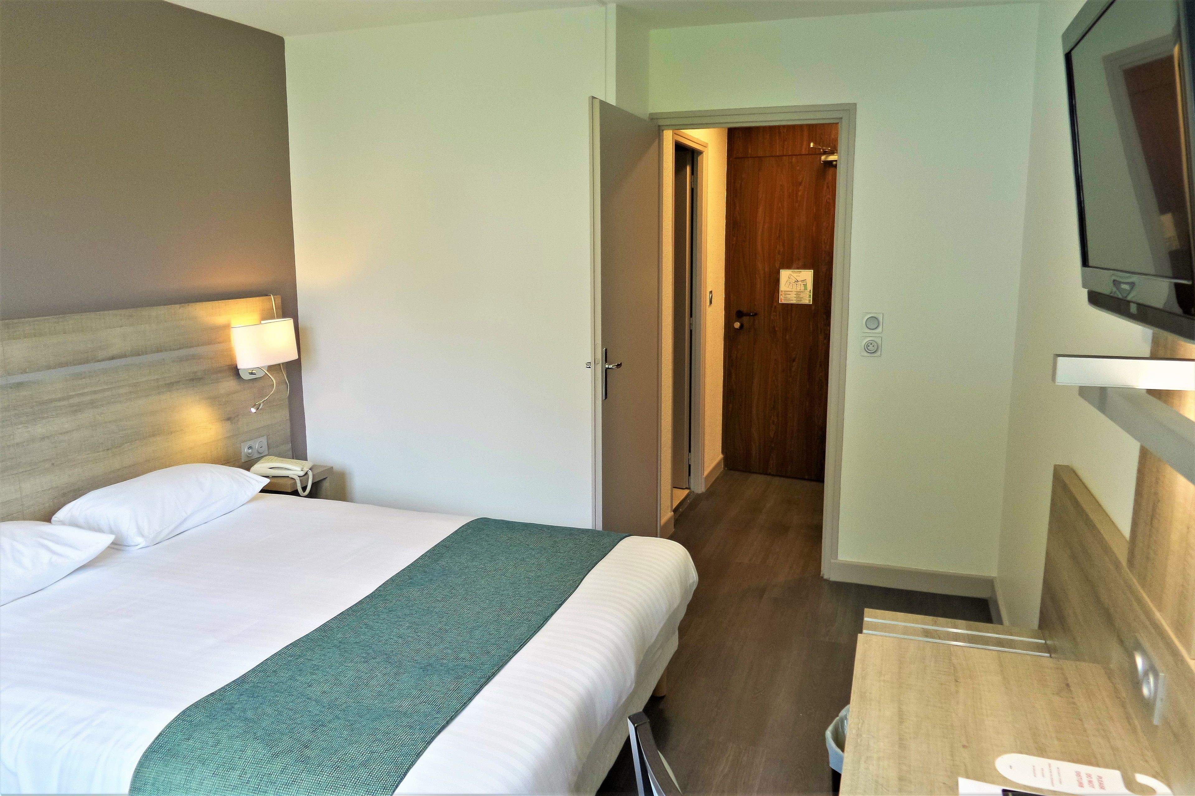 Een hotelkamer met een bed, een bedlampje en een aan de muur bevestigde televisie.