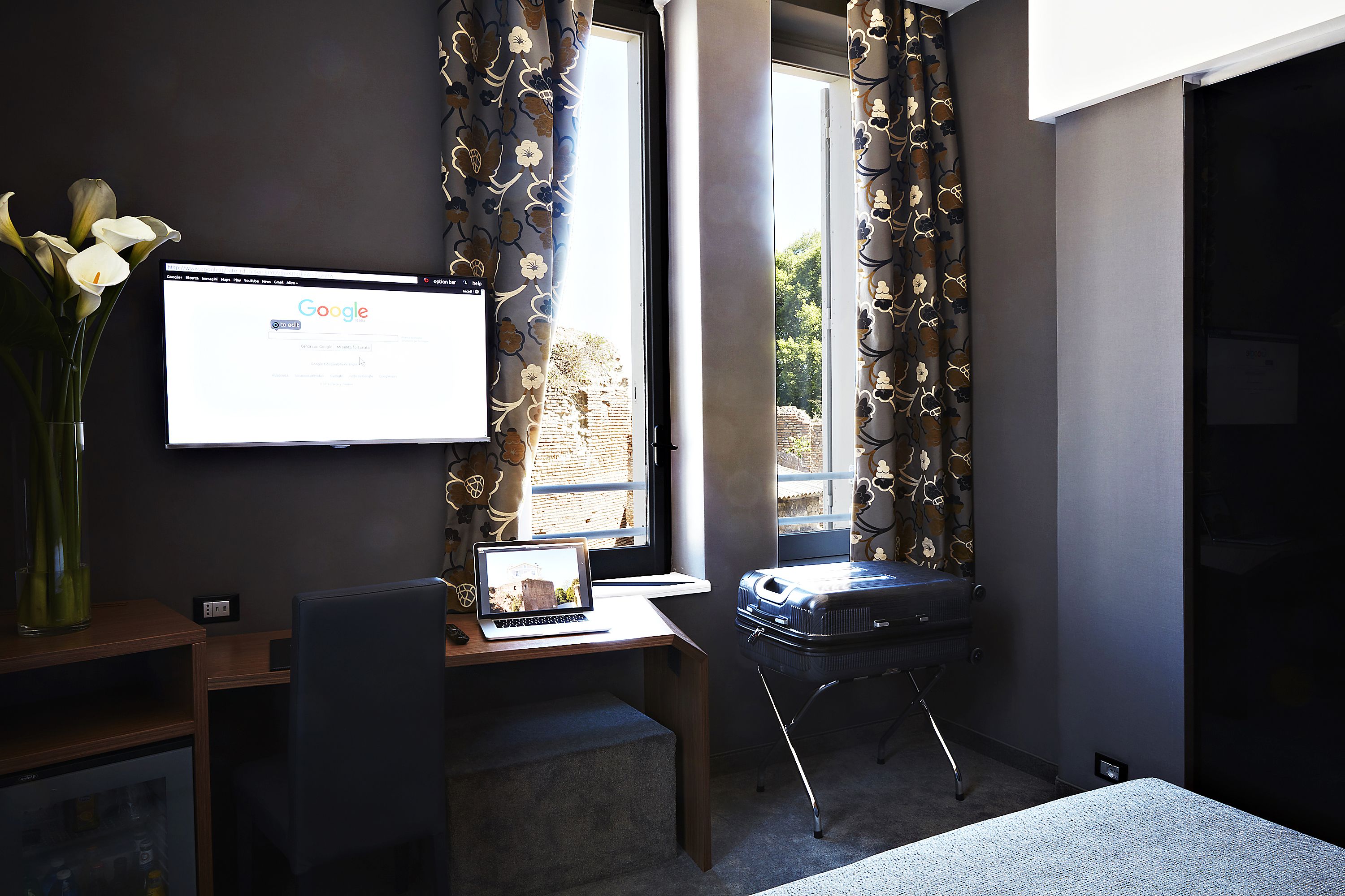 A hotel room with a desk, laptop, and a suitcase.