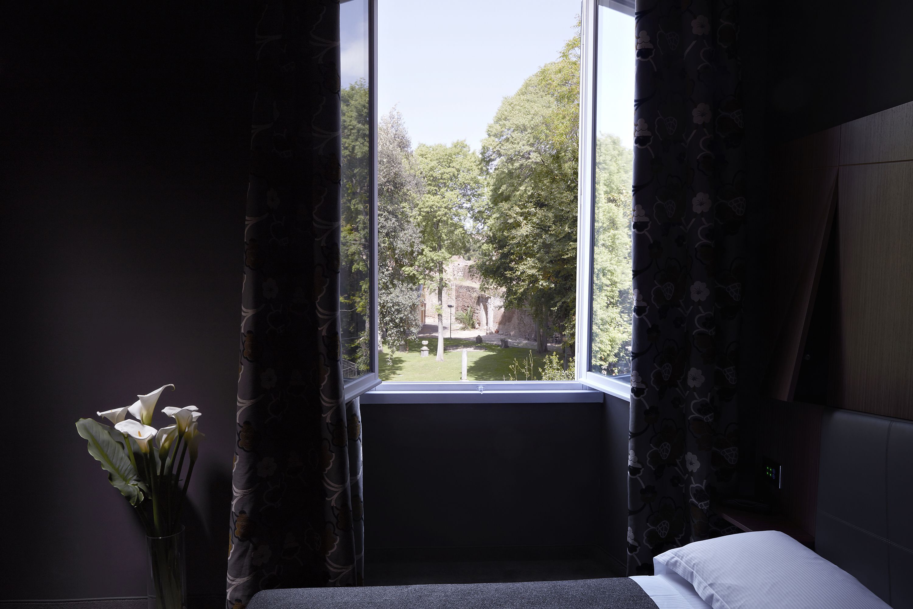 A room with a bed, a window with curtains, and a vase with flowers.