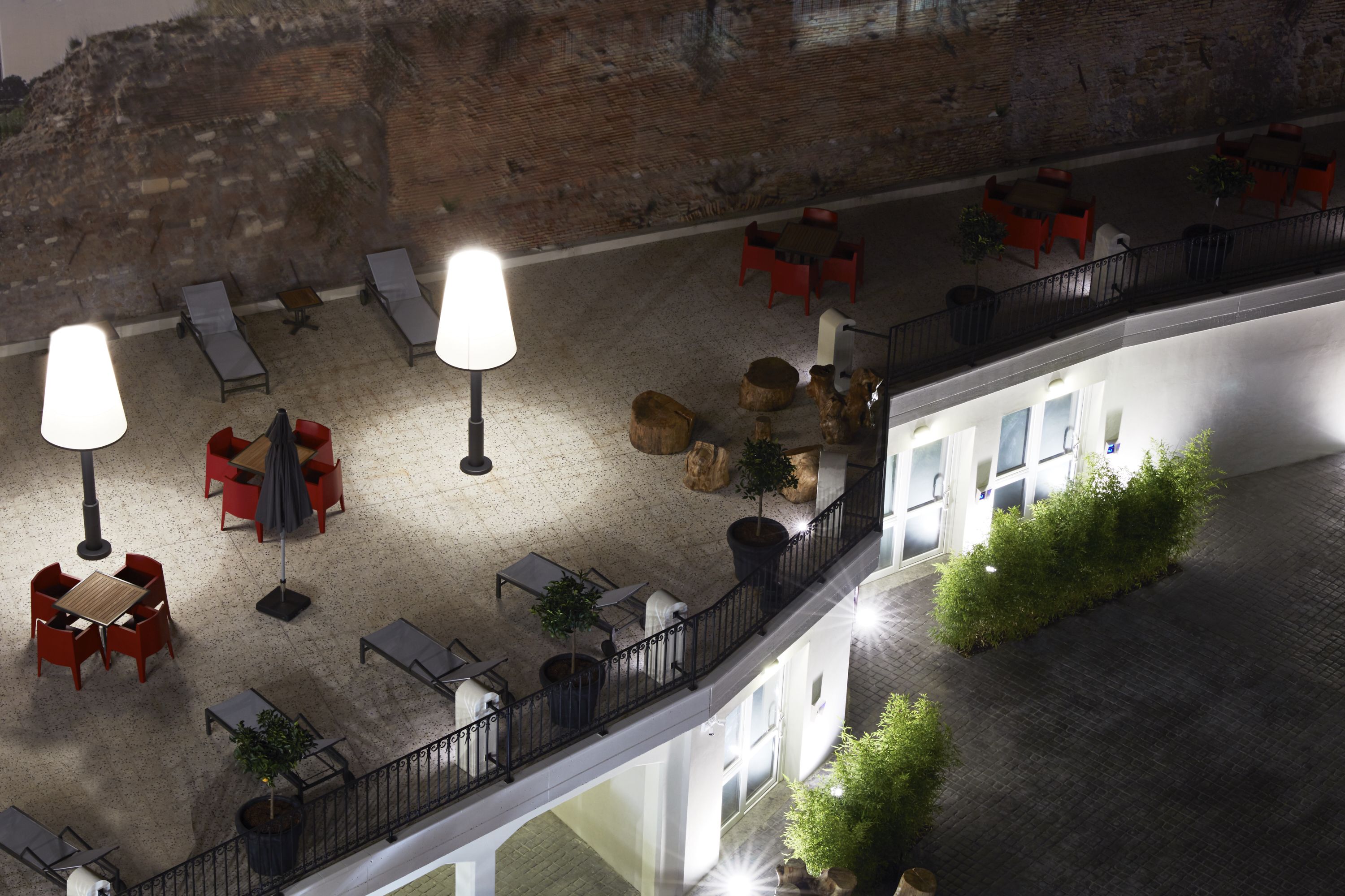 An outdoor terrace with seating and tables, a brick wall, and a balcony railing.